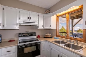 A kitchen with white cabinets, a stove, a sink, and a window with a view of trees and mountains. - Aspen View (Blowing Rock)