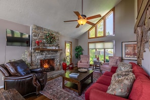 A living room with a stone fireplace, leather sofa, red armchair, and a ceiling fan. - Aspen View (Blowing Rock)