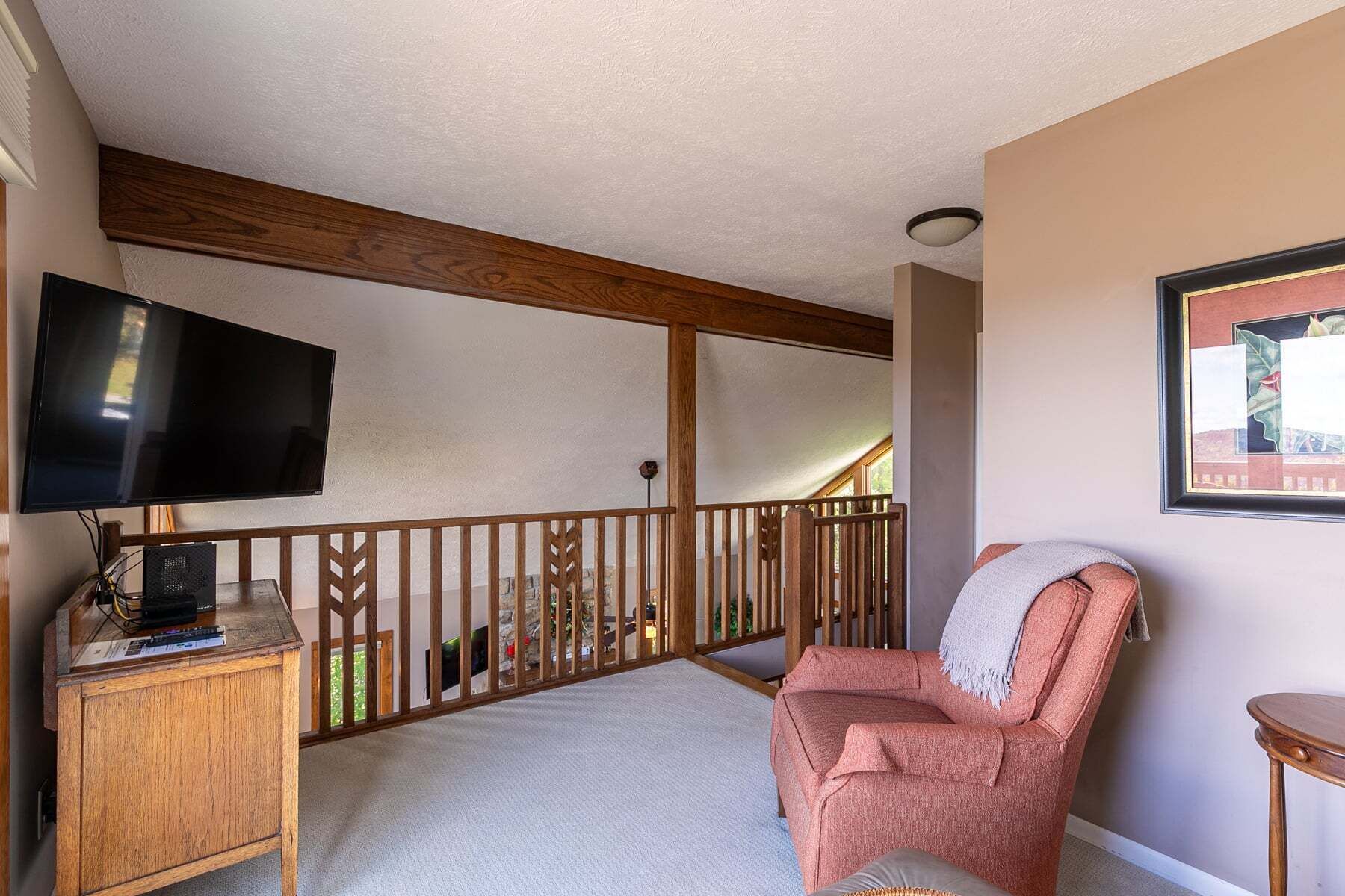 A room with a wooden ceiling, a television on a stand, a chair with a blanket, and a small table.