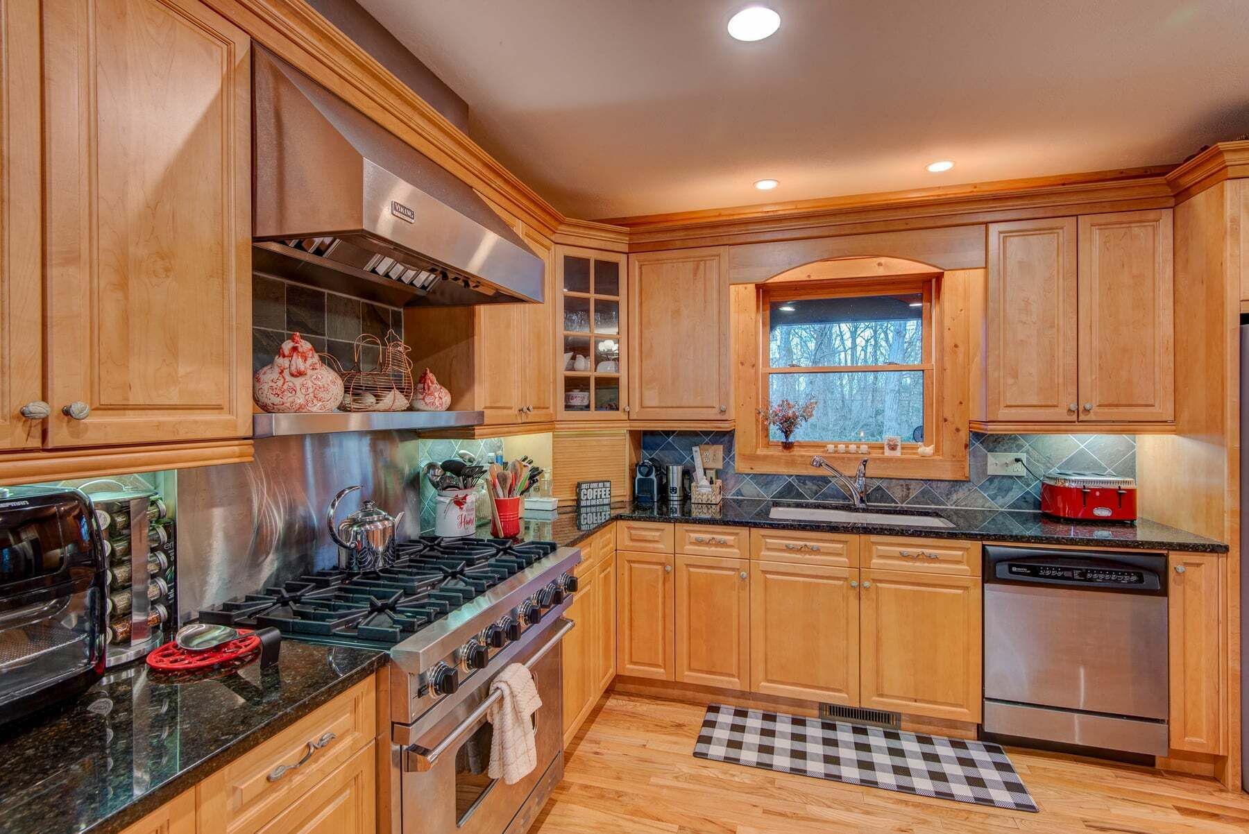 A kitchen with wooden cabinets, a stove, a dishwasher, and a window with a view.