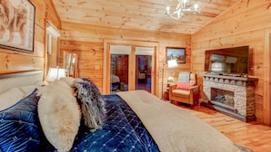 A wooden cabin interior with a bed, a fireplace, and a ceiling light. - Blueberry Hills 3BR With hot Tub, pet Friendly, Outdoor Fireplace (Boone)