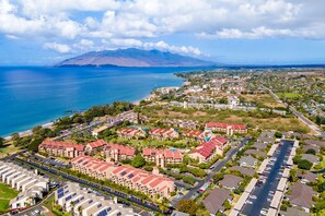 An aerial view of a coastal residential area with apartment buildings, roads, and a large body of water. - Kamaole Sands 5-210 (Kihei)
