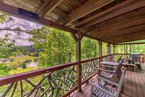 Um deck de madeira com guarda-corpo, móveis de exterior e vista para uma paisagem verde.