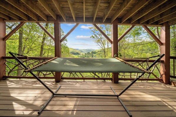 Une terrasse en bois avec un hamac et une vue sur une vallée boisée.