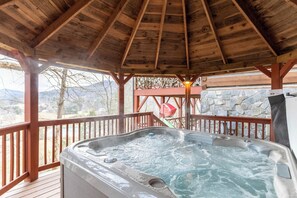 Une terrasse en bois avec un jacuzzi, un mur en pierre et une vue sur les montagnes.