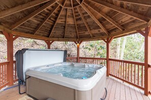 Un bain à remous installé sous une pergola en bois, avec une terrasse en bois et des garde-corps.