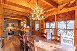 Un intérieur en bois comprenant une table à manger, des chaises, un lustre et un coin cuisine.