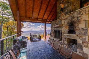 A covered outdoor seating area with a stone fireplace, wicker furniture, and a view of the mountains. - Heavenly Daze at Eagles Nest (Banner Elk)
