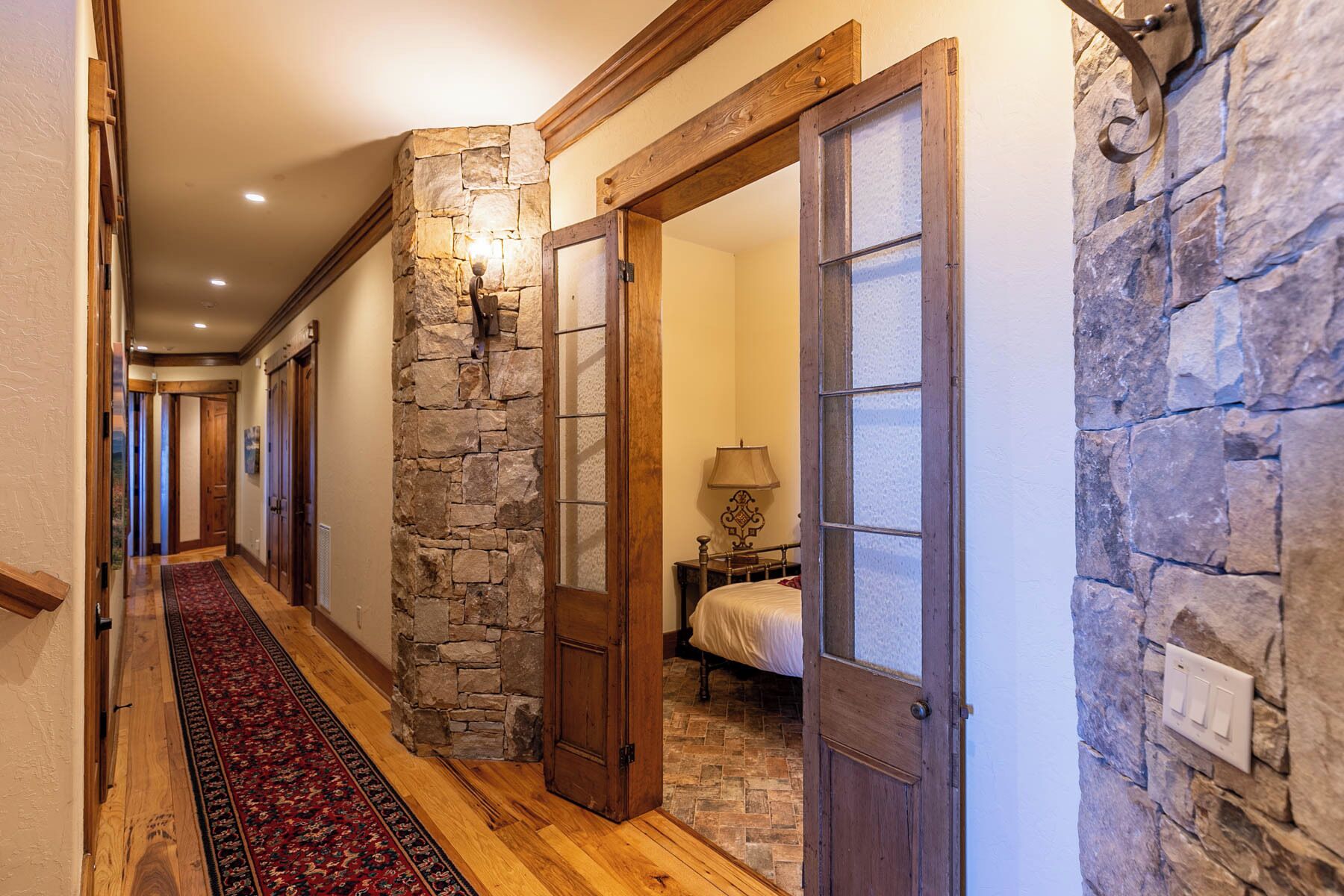 A hallway with stone walls, wooden doors, and a red carpet.