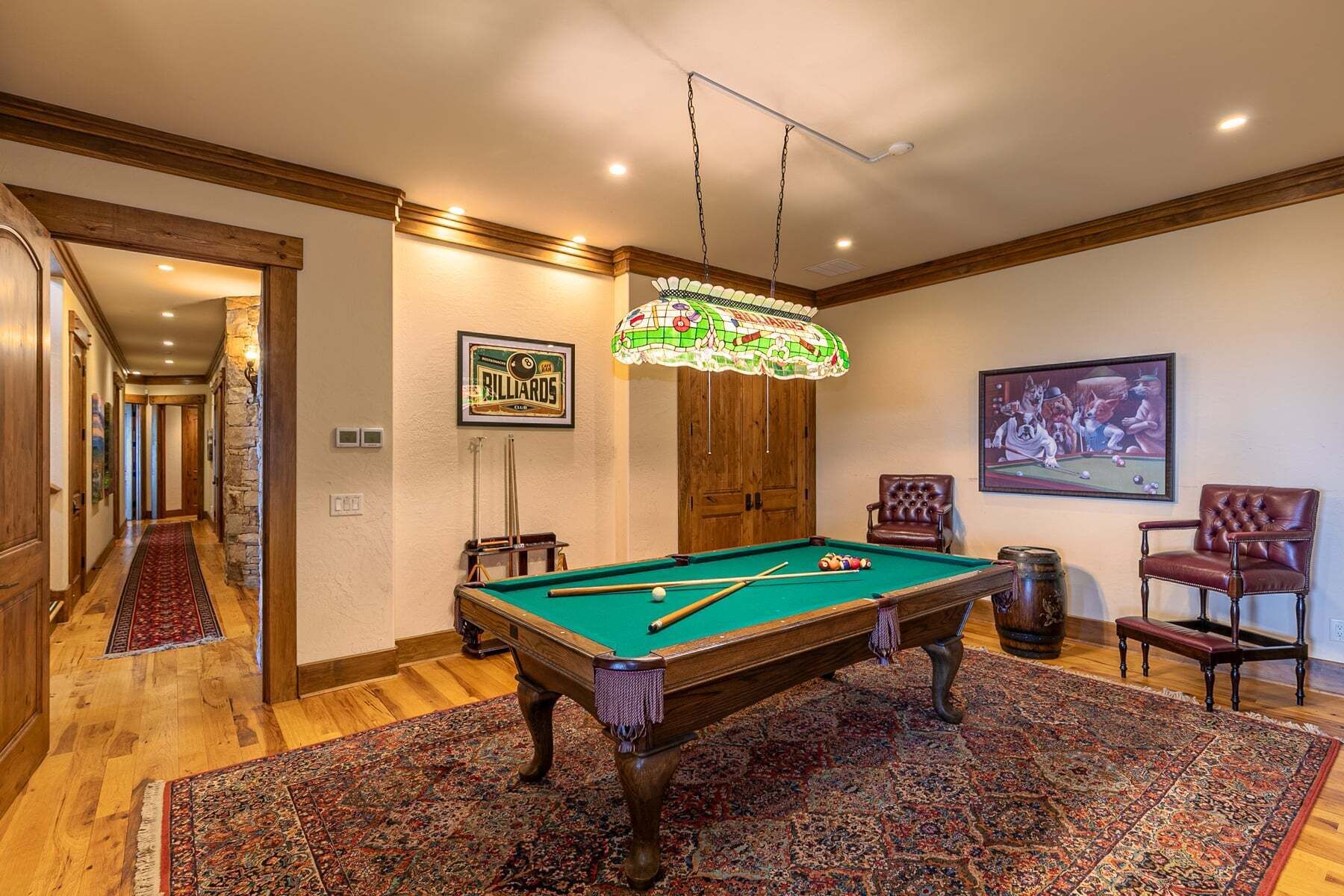 Une table de billard dans une pièce dotée d’un plancher en bois, d’un tapis à motifs, d’une décoration murale sur le thème du billard et d’un tableau encadré représentant des personnages de dessins animés jouant au billard.