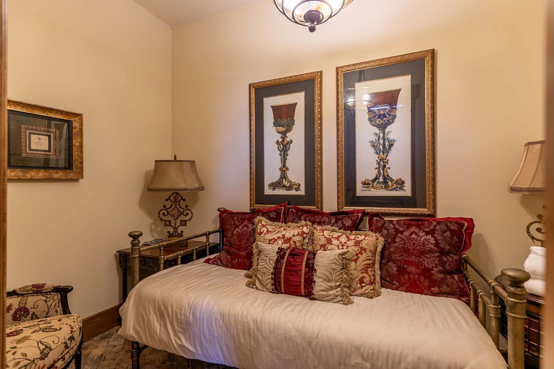 Une pièce avec un lit, deux tableaux encadrés au mur, une lampe et une chaise.