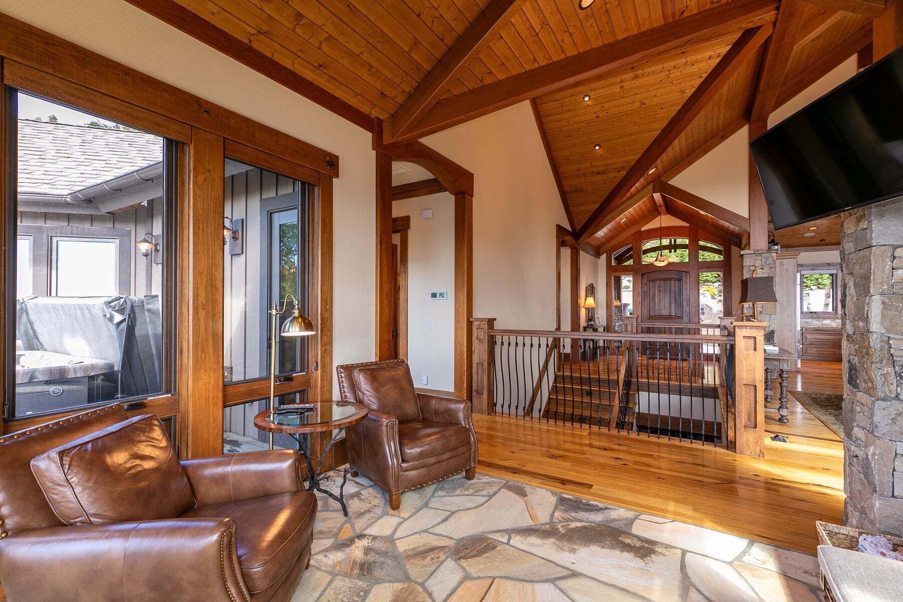 A spacious living area with leather sofas, a stone floor, wooden beams, and a stone fireplace.