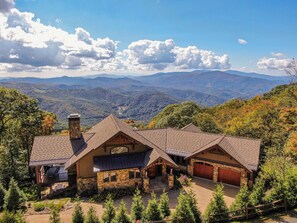 A large, stone cabin with a sloped roof, surrounded by a forested landscape and mountains in the background. - Heavenly Daze at Eagles Nest (Banner Elk)