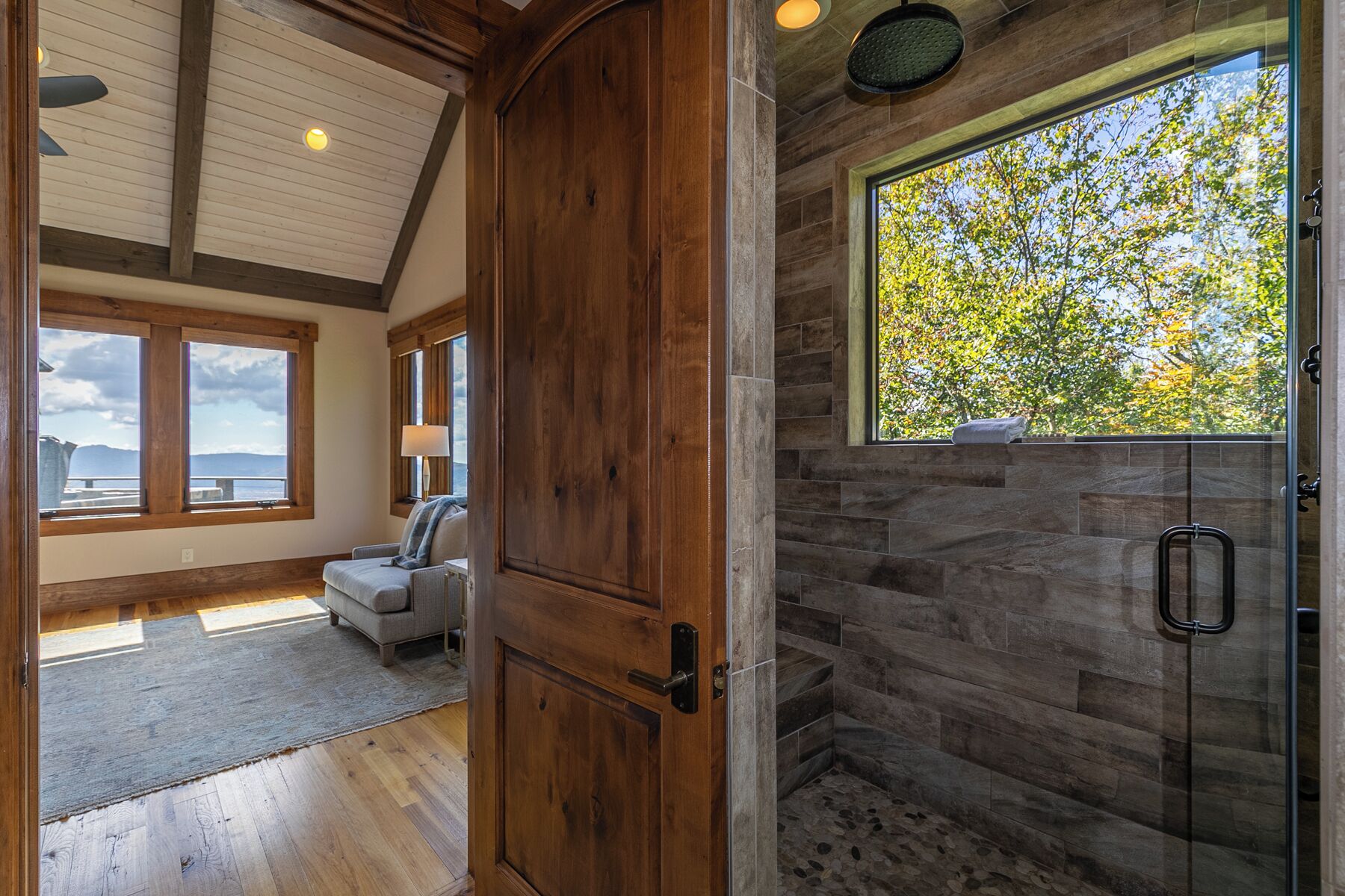 A spacious room with a large window, a wooden door, and a stone shower area.
