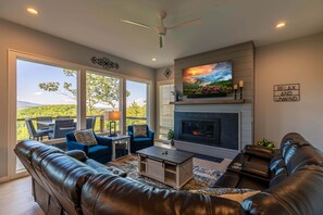 A living room with a fireplace, leather sofas, a coffee table, and a TV mounted above the fireplace. - Blue Ridge Sanctuary at Blue Ridge Mountain Club (Lenoir)