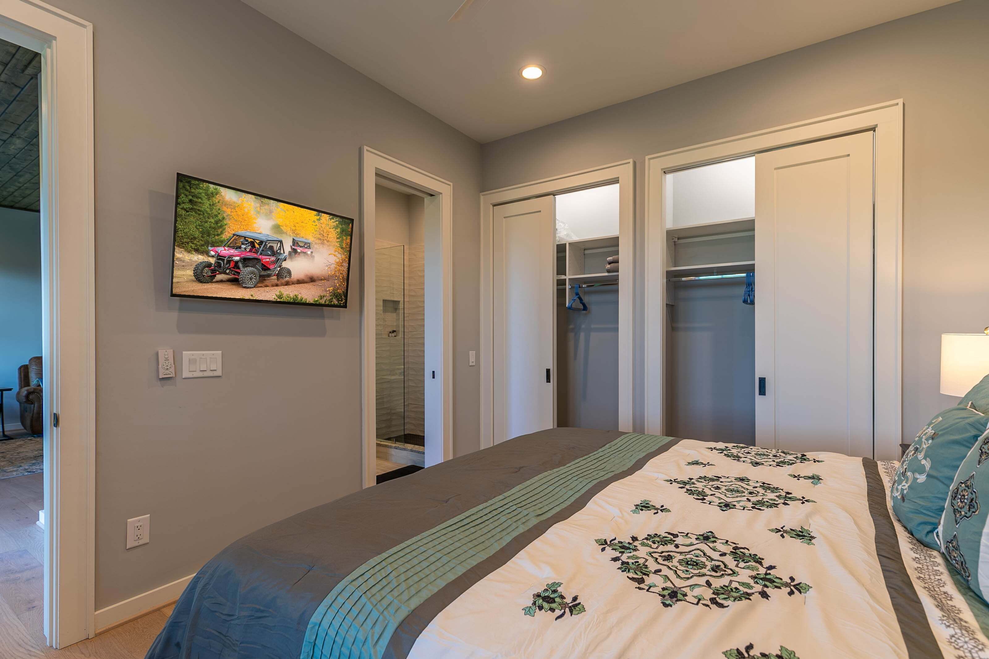A bedroom with a bed, a television on the wall, and a closet with sliding doors.