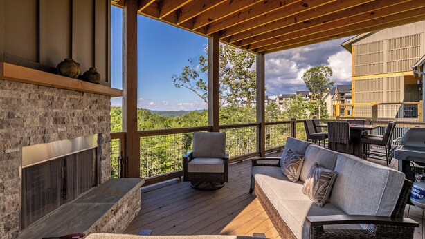 A covered outdoor deck with a stone fireplace, seating area, and a view of the surrounding landscape. - Blue Ridge Sanctuary at Blue Ridge Mountain Club (Lenoir)