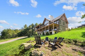 A large, multi-story lodge with a prominent balcony, outdoor seating area with Adirondack chairs, and a well-maintained lawn. - The Tipsy Bear at Eagles Nest (Elk Park)