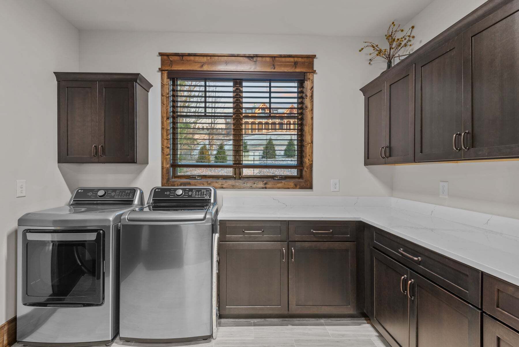 A kitchen with a built-in washer and dryer, wooden cabinets, and a window with a view of houses.