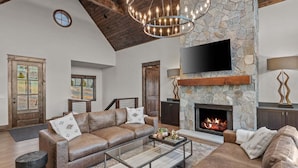 Un salón espacioso con chimenea de piedra, sofás de cuero, una mesa de centro de cristal y un televisor montado en la pared.