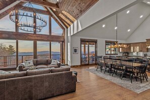 A spacious living area with a large window, a wooden ceiling, and a dining area with chairs and a table.