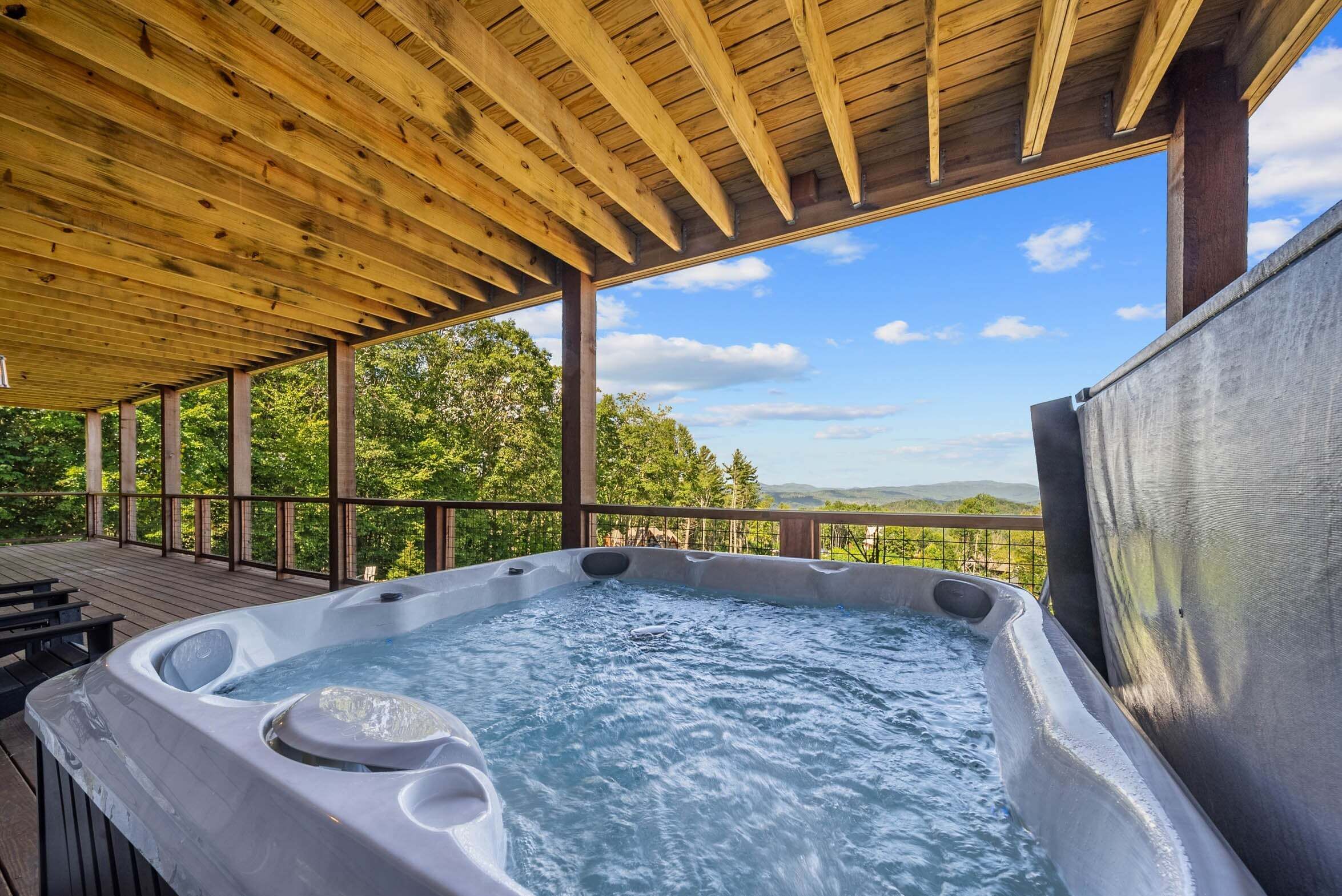 A hot tub under a wooden pergola with a view of trees and mountains.