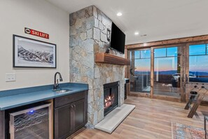 A modern kitchen with a stone fireplace, a ski lift sign, and a large window overlooking a scenic view.