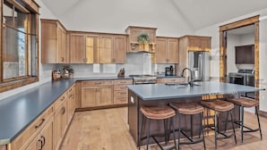 Una cocina amplia con armarios de madera, una isla central con taburetes, electrodomésticos de acero inoxidable y un ventanal grande.