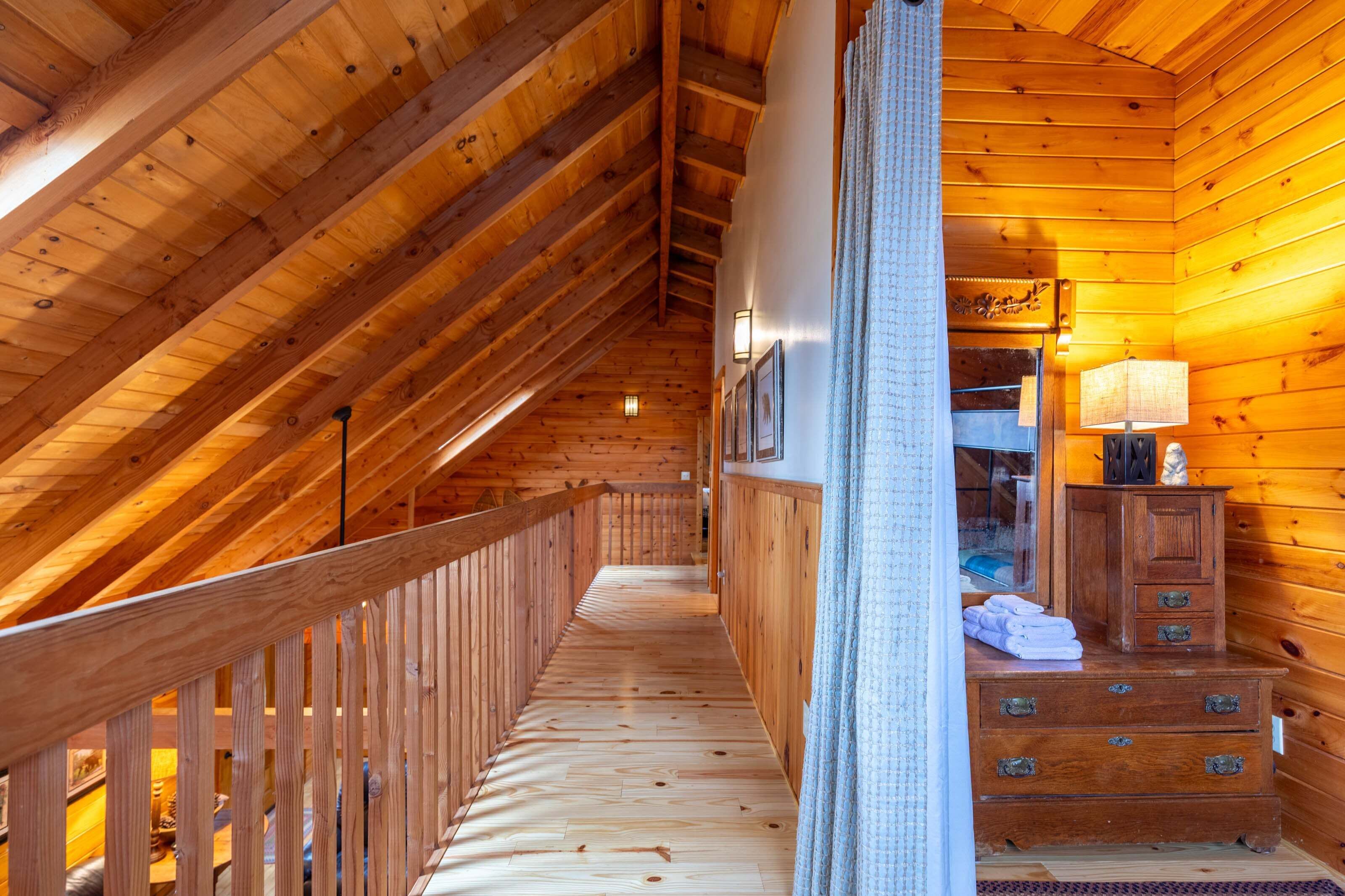 Interior de madera con techo inclinado, barandal de madera, escalera y un mueble con toallas.