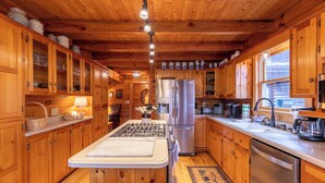 A wooden cabin kitchen with a central island, stainless steel appliances, and wooden cabinets. - Weathering Heights (Boone)