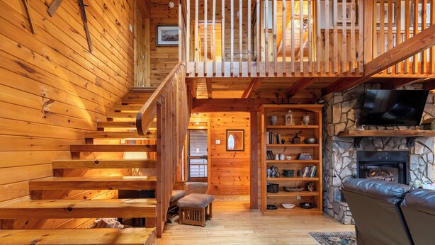 A wooden interior with a staircase, a stone fireplace, and a television. - Weathering Heights (Boone)