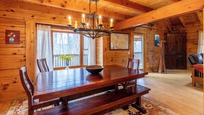 A wooden interior with a dining table, chairs, a chandelier, and a large window. - Weathering Heights (Boone)
