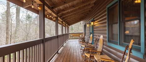 A wooden deck with chairs and tables, a wooden ceiling, and windows with curtains.
