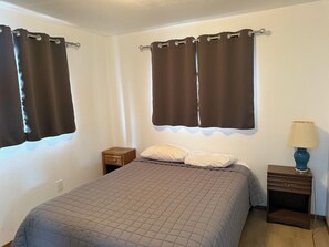 Quarto com cama, duas mesas de cabeceira, abajur e cortinas.