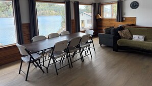 A room with a dining table, chairs, a sofa, a ceiling fan, and large windows with curtains.