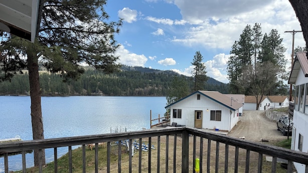 A lakeside cabin with a deck, a dock, and a view of the lake and mountains.