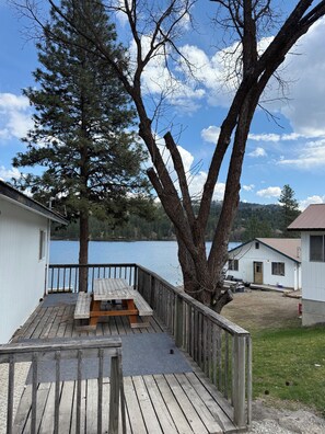 Eine Holzterrasse mit einem Picknicktisch, ein kleines GebĂ€ude mit einer TĂŒr und ein groĂer Baum.