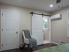 A room with two white doors, a chair, a window, and an air conditioning unit.
