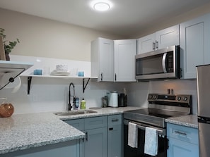 A modern kitchen with white cabinets, a built-in microwave, a stove, and a sink.