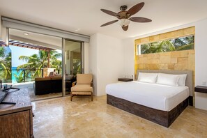Ein Schlafzimmer mit Bett, Stuhl, Nachttisch, Deckenventilator, einer Schiebetür zu einem Balkon und einer Steinwand mit Fenster.