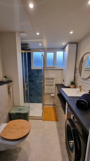 Une salle de bain compacte comprenant une douche en verre, des toilettes, un lave-linge et un lavabo avec un miroir.