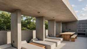 Een moderne buitenruimte met betonnen pilaren, beklede banken en een houten tafel.