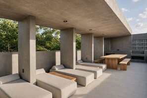 A modern outdoor seating area with concrete pillars, cushioned benches, and a wooden table. - Romantic Jungle Studio, Rooftop Pool & Lounge Fast WIFI/AC in Tulum (Tulum)