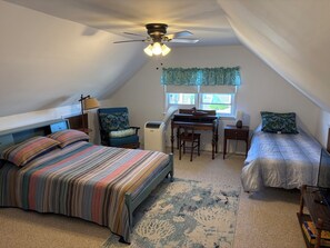 A bedroom with a bed, a desk, a chair, a ceiling fan, and a window with curtains.