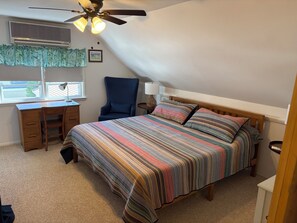 A bedroom with a bed, desk, chair, and a ceiling fan.