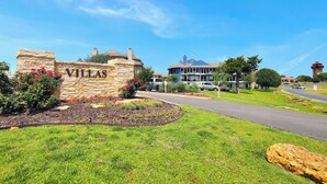 A stone sign with 'Villas' written on it, a well-maintained lawn, a road, and a building with a blue roof in the background. - 3 Bedroom Lake Escape steps to resort & marina (Pottsboro)