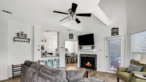 A living room with a gray sectional sofa, a green armchair, a fireplace, a ceiling fan, and a TV mounted on the wall. - 3 Bedroom Lake Escape steps to resort & marina (Pottsboro)