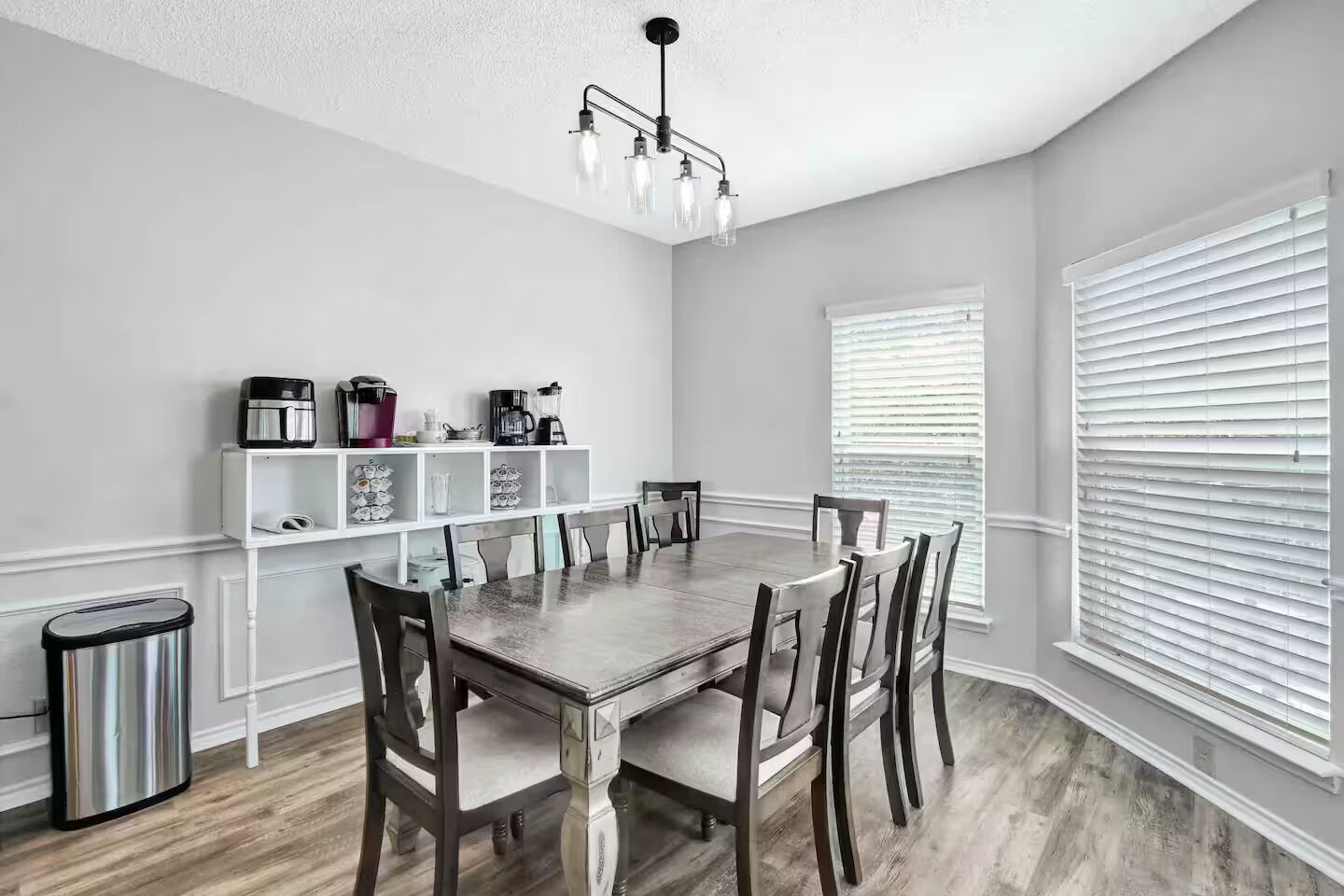 A dining area with a wooden table, chairs, a chandelier, and a coffee station.