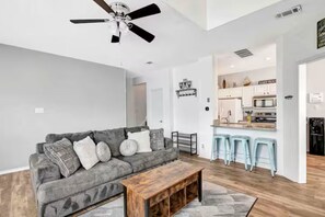 Un salon moderne avec un canapé gris, une table basse en bois et un ventilateur de plafond.