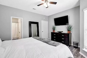 A bedroom with a bed, a ceiling fan, a dresser, a TV, and a door.